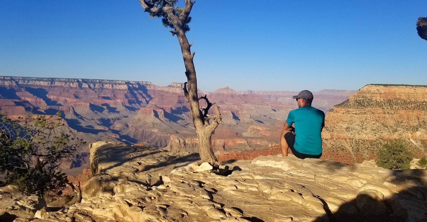 Manny sitting on a rock ledge looking out over the Grand Canyon at sunset