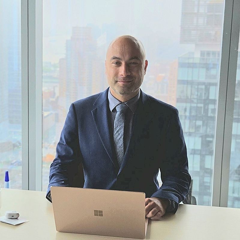 Manny seated at a desk with a laptop in front of a high-rise window